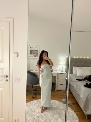 Ljusblå långklänning med rosetter - Säljer en elegant ljusblå långklänning med axelbandslös design och snygga rosetter längs sidan. Klänningen har en slits bak och är figurnära med cut-out detaljer vid midjan. Perfekt för dig som vill sticka ut med en stilren look. Endast använd 2 gånger💙