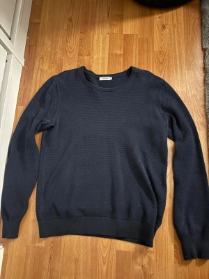Mörkblå stickad tröja J.Lindeberg M - Snygg mörkblå stickad tröja från J.Lindeberg i storlek M. Tröjan har ett diskret strukturerat mönster och rund hals. Ribbstickade muddar vid ärmslut och nederkant ger en clean look. Perfekt för dig som gillar stilrena och klassiska plagg. Den är använd men fortfarande i bra skick. Priset kan även diskuteras via snabb affär👍👍