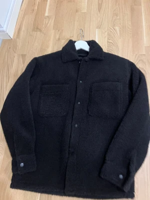 Svart klassisk cost  - Knappt använt Mjuk och fluffig svart klassisk coat med två stora bröstfickor och knappar framtill. Jackan har klassisk krage och långa ärmar med knappdetalj vid mudden. Perfekt för dig som gillar chill och stilren vibe, storleken gå oversize och är på storlek xs mening att det passa S perfekt …. Kvinnor kan också ha de på dom är otroligt snygga:)