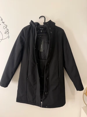 Svart parkajacka från Vero Moda - Svart parkajacka från Vero Moda med huva och dragkedja framtill. Jackan har en clean look med långa ärmar och diskreta fickor på sidorna. Perfekt för dig som gillar stilrena och funktionella ytterplagg. Materialet är syntet och jackan har normal passform. Storlek XXS Petite modell