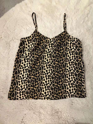 Leopardmönstrad linnetopp Vero Moda - Säljer en snygg leopardmönstrad linnetopp från Vero Moda i storlek S. Toppen har tunna axelband och är i beige och svart med bruna inslag. Materialet är mjukt och lätt polyester, perfekt för att ge din outfit lite edge.