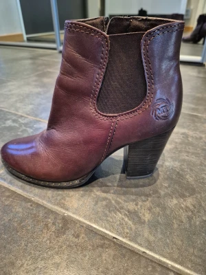 Marco Tozzi, Bruna stövletteri - Knappt använda bruna  stövletter från Marco Tozzi stabil hög klack. Skorna är i skinn med elastiska paneler på sidorna och dragkedja för enkel påtagning. 