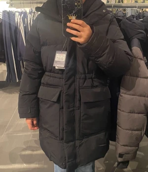 Svart lång pufferjacka med huva - säljer en lång svart jacka, den är i bra skick förutom ett litet 5 mm hål på baksidan av den ”kan sy den (syns knappast) men har bara haft på mig den 1 gång vilket den då fastnade i ett galler och gick tyvärr sönder (jag kan skicka tydligare bilder om ni önskar och ja säljer för 600 nypris var 1000 som syns i bilden)