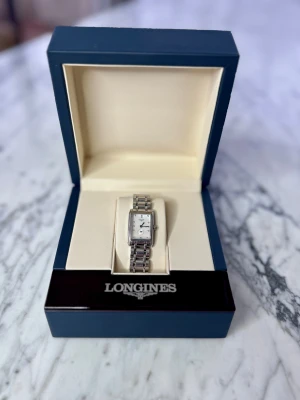 Longines DolceVita Watch - Elegant Longines DolceVita in polished stainless steel, featuring a rectangular case and a white dial set with 12 diamond hour markers. Classic blue steel hands and a small-seconds subdial add that signature Longines refinement.  Model ref. L5.255.4 with serial 49755115. Swiss quartz movement. Original stainless steel bracelet. Light signs of wear but overall in great pre-loved condition — the dial and diamonds look stunning. The boet has a measurement of 20.8x32mm. 