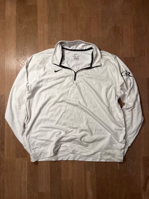 Vit Nike Dri-Fit half zip tröja - Säljer en riktigt snygg vintage långärmad Nike Dri-Fit tröja med half zip och svart Nike-logga på bröstet. Tröjan har en hög krage med svart kant och GR-brodyr på ena ärmen. Perfekt för träning eller chill. Sitter bra som L men det står XL  Skick 8/10 behöver sig en tvätt ✅ Skickar inom 48 timmar om inte samma dag 🚚