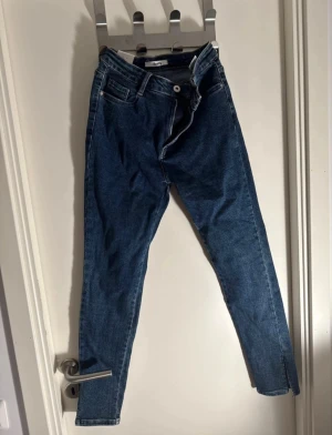 Blå jeans med slits  - Säljer dessa snygga mörkblå jeans med trendiga slitsar vid anklarna. Aldrig använda.  •Helt nya med prislapp •Mjuk och stretchig denim för en bekväm passform Står XL/42 på dem men de passar mer som en L