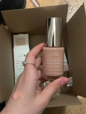 100% Pure Fruit Pigmented Water Foundation - Hydrerande foundation i nyansen Cool 1.0 med fruktpigment, vegansk och cruelty free. Ger full täckning och en lätt daggig finish. Kommer i en snygg glasflaska med silvrig kork, 30 ml. Naturlig, glutenfri och giftfri formula. Den är helt ny bara testad! Säljer den pågrund av att färgen passade mig tyvärr inte.