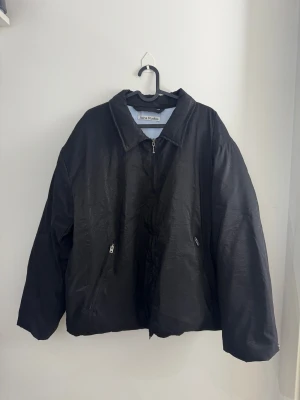Svart puff jacka från Acne Studios i storlek S - Säljer en svart puffer jacka från Acne Studios med oversized passform. Jackan har dragkedja framtill, två snedställda fickor med dragkedja och klassisk krage. Materialet är lätt och har en diskret glans. Perfekt för dig som gillar minimalistisk och clean stil.