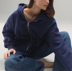 Marinblå hoodie med dragkedja - Säljer en marinblå hoodie med huva och hel dragkedja framtill. Tröjan har en loose passform, ribbade muddar och en stor ficka på magen. Perfekt för chill dagar och enkel att matcha med jeans eller joggers. Endast använd fåtal gånger