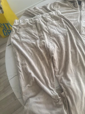 Beige mjukisbyxor med snörning - Säljer ett par beige mjukisbyxor med snörning i midjan och två bakfickor. Byxorna är tillverkade i ett mjukt och lent material som känns skönt mot huden. Passformen är loose och de har en enkel, stilren look som funkar perfekt för chill dagar.