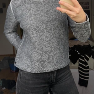 Grå blommig stickad tröja från Hugo Boss - Säljer en grå stickad tröja från Hugo Boss med blommigt mönster. Tröjan har rund halsringning och långa ärmar. Perfekt för dig som gillar en stilren men ändå detaljrik look.