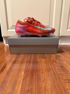 Nike Mercurial Vapor 16 Elite Fg - Tja! Säljer ett par Nike Mercurial Vapor 16 Elite Fg i färgen röd/rosa med turkos swosh. Super fin färg perfekt för dig som vill sticka ut lite mer på plan. Skick: 7/10 använda typ en hel säsong har 2 defekter en liten bit på framsidan på högerskon har gått bort lite påverkar inget sen är det uppe vid vänsterskon där har det gått sönder lite det är inte jätte stort. Storlek: 40. Pris: 499kr köpta för 3399kr på stadium. Pris kan diskuteras vid snabbaffär💨Kom DM vid fler bilder eller funderingar🥰