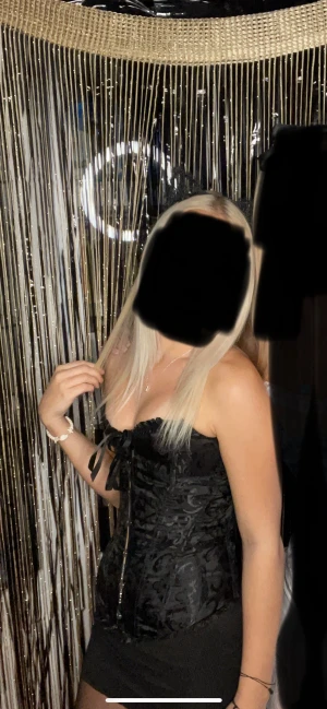 Svart korsett med snörning och mönster - Säljer en svart korsett med snyggt ton-i-ton mönster och snörning framtill. Toppen har en figurnära passform, volangkant upptill och är axelbandslös. Perfekt för dig som vill ha en edgy och trendig look.