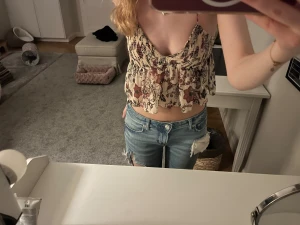 Blommig croppad linnetopp med volang - Säljer en blommig croppad linnetopp med volangkant och smala axelband. Toppen har v-ringning och ett romantiskt mönster i beige, vinrött och lila. Perfekt för varma dagar och ger en söt och avslappnad vibe.