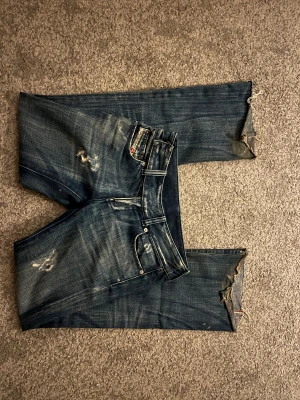 Blå Diesel jeans med slitningar - Säljer ett par blå jeans från Diesel med coola slitningar och tvättade detaljer. Säljer eftersom de inte längre kommer till andvändning, jag är 163ish och de e lite långa på mig! Pris går att diskutera. De är i bra skick förutom att de är slitna längst ner, då de nästan är oundvikligt utomhus. 
