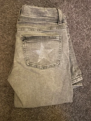 Grå bootcut jeans från Gina Young - Snygga grå jeans från Gina Young i bootcut-modell med låg midja och snygg stjärndetalj på ena bakfickan! 🌟 Jeansen är i strl 170 och längden passar mig som är 165cm perfekt!😍Jag säljer de pga att de kommit till användning för sällan (ca 3 gånger) Hör av dig för fler frågor❣️