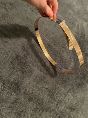 Guldigt metallbälte i minimalistisk stil - Säljer ett stilrent bälte i guldig metall med slät, blank yta och enkel design. Bältet är smalt och har en modern, minimalistisk look som verkligen sticker ut. Perfekt för att ge outfiten en extra touch av elegans och edge.