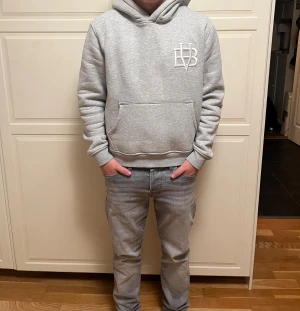 Grå hoodie från bvaldi - Snygg grå hoodie från bvaldi med  vit broderad logga på bröstet. Tröjan har huva, magficka och ribbade muddar vid ärmslut och nederkant. Perfekt för chill dagar och enkel att matcha med jeans eller joggers.