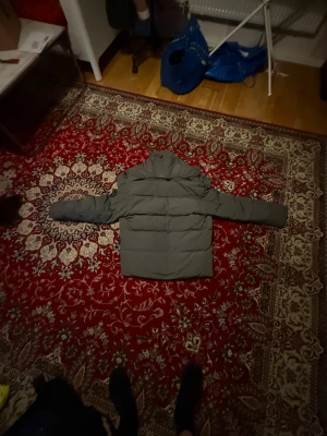 Grå pufferjacka från Canada Goose - Säljer en grå pufferjacka från Canada Goose i storlek L. Jackan har hög krage, långa ärmar och flera fickor framtill. Stängs med både dragkedja och knappar. Insidan är svart och jackan är fodrad för extra värme. Perfekt för kalla dagar.