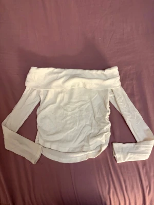 Vit offshoulder långärmad topp - Säljer en vit offshoulder topp med långa ärmar. Toppen har en bred kant upptill som ger en snygg och trendig look. Materialet känns mjukt och stretchigt, perfekt för dig som gillar stilrena och enkla plagg. Passar dig som vill ha en clean och fräsch vibe.