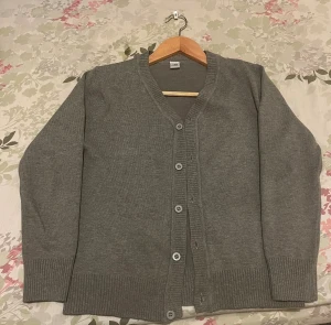 Grå kofta med knappar - En enkel och stilren grå kofta med ribbade muddar och knappstängning framtill. Koftan har långärmade och är tillverkad i ett mjukt stickat material som känns skönt mot huden. Perfekt att slänga på sig när det är lite kyligt ute.