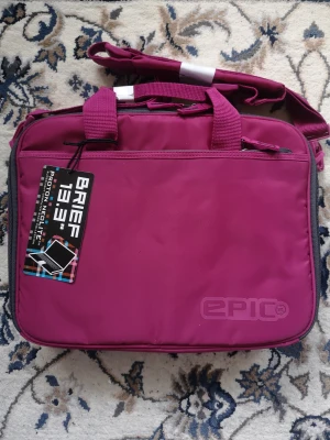 Julklappstips! Vinröd datorväska från Epic - Mptt:34*26*6cm. Snygg och praktisk datorväska med handtag och justerbar axelrem. Materialet är slitstark polyester och väskan har dragkedja upptill, finns flera fack för förvaring. 