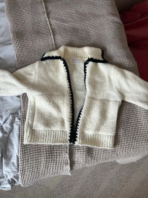 Vit stickad kofta från Zara - Mysig vit stickad kofta från Zara med svarta detaljer längs krage, ärmslut och öppning.  Säljer denna för att den blev tyvärr för liten för mig!