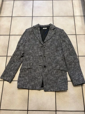 Svartvit kavaj från Emanuelli - Säljer en svartvit kavaj från Emanuelli med snyggt vävt mönster. Kavajen har tre knappar framtill, klassisk krage och två fickor. Fodrad insida för extra komfort och stilren look. Perfekt för dig som vill ha en tidlös och trendig vibe.