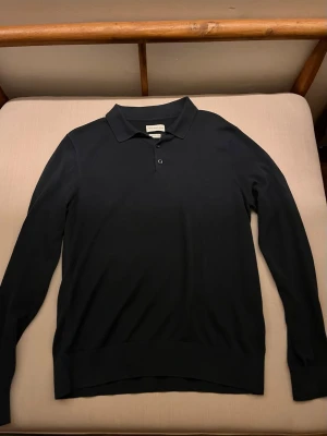 Svart långärmad henley från These Glory Days - Klassisk svart långärmad henley från These Glory Days i mjuk bomull. Skjortan har krage, knappar framtill och en clean, stilren look som passar till allt. Perfekt för dig som gillar minimalistisk stil och vill ha något enkelt men snyggt.