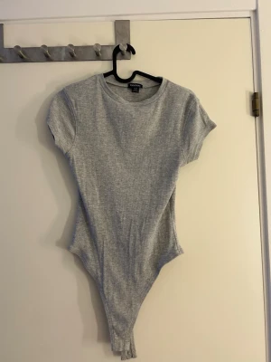 Grå ribbad bodysuit från Boohoo - Säljer denna body som aldrig kommit till användning, så den är i nyskick! Materialet är ganska stretchigt. Den är köpt från Boohoo och är i storlek 38 m. 