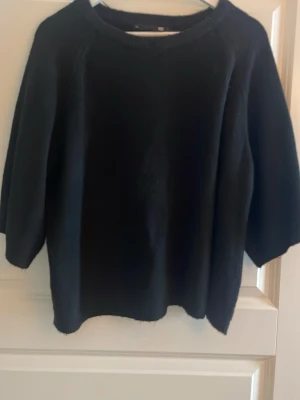 Svart stickad tröja med trekvartsärm - En enkel svart stickad tröja med rund hals och trekvartsärm. Tröjan har en rak passform och är perfekt för lager på lager under kyligare dagar. Mjuk och bekväm, passar till det mesta i garderoben.