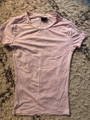 Ljusrosa basic t-shirt - En enkel och stilren ljusrosa t-shirt med rund hals och korta ärmar. Tillverkad i mjuk bomull som känns skön mot huden. Perfekt att matcha med jeans eller shorts för en clean look.