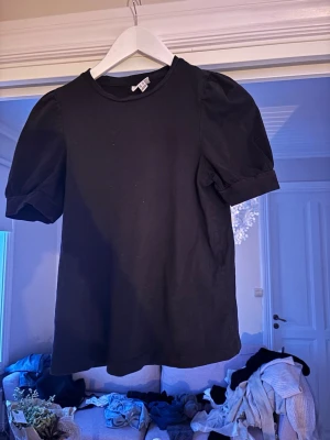 Svart puffärm topp  - En svart topp med puffärmar och rund halsringning. Toppen är mjuk och har en enkel, stilren design som passar till många olika outfits. Perfekt för dig som gillar en klassisk look med en twist.