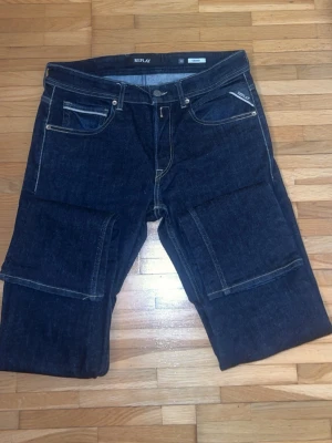 Replay Grover jeans mörkblå denim - Mörkblå Replay Grover jeans med klassisk femficksdesign och kontrastsömmar. Snygga raka ben och tydlig logga på bakfickan samt läderpatch i midjan. Tillverkade i robust denim med detaljerade sömmar och coola bakfickor.