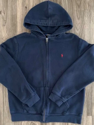 Polo Ralph Lauren zip hoodie – marinblå – fint skick - Klassisk Polo Ralph Lauren zip hoodie i marinblå färg. Stilren design med broderad logga på bröstet. Mjuk och bekväm, perfekt för både vardag och skola. Fint skick utan hål eller fläckar. Passar alla outfits och årstider. Snabb affär prioriteras. OBS XL 16/18 år