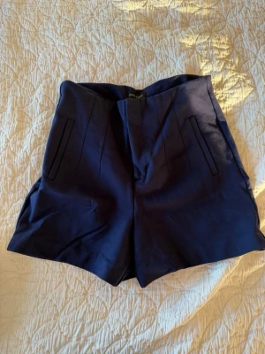 Mörkblå shorts från Anna Field - Snygga mörkblå shorts från Anna Field i storlek XL. De är högmidjade med raka ben och har två diskreta fickor framtill. Materialet känns mjukt och har en lätt stretch, perfekt för varma dagar. Klassisk och stilren design som är enkel att matcha.