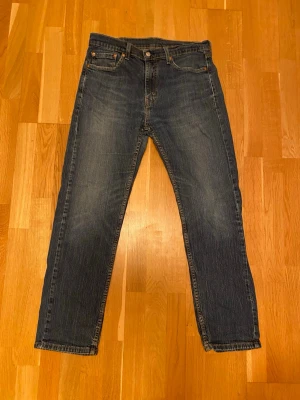 Levi's 505 raka blå jeans W33 L32 - Klassiska Levi's 505 jeans i blå denim med raka ben och normal passform. Jeansen har fem fickor, gylf med dragkedja och tydliga kontrastsömmar. Perfekta för dig som gillar tidlös stil och vill ha ett par slitstarka jeans.