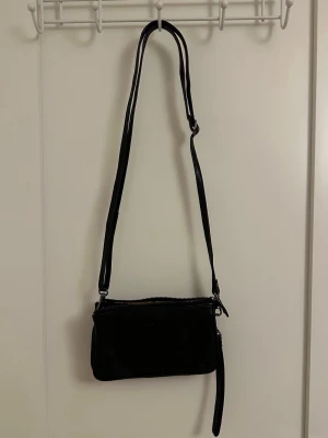 Svart axelväska från CASSÉL - Säljer en stilren svart axelväska från CASSÉL. Väskan har justerbar axelrem, dragkedja upptill och flera fack inuti. På framsidan kan man se att en katt har klöst lite, men det är iallafall inget jag tänker på då man inte ser de speciellt mycket.  