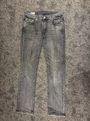 Levi's 514 grå jeans, W30 L32 - Säljer ett par Levi's Premium 514 jeans i grå tvätt. Klassisk femficksmodell med raka ben och normal passform. Jeansen har snygga slitningar och detaljer i silverfärgad metall. Perfekta för dig som gillar en stilren look.