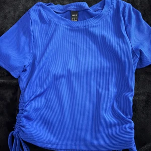 Blå ribbad topp  - Säljer en blå ribbad topp från SHEIN med korta ärmar och rund hals. Toppen har snörning i sidan som ger en snygg detalj och gör att du kan justera passformen. Perfekt till jeans eller kjol för en trendig look.