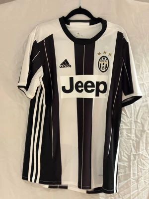 16/17 Juventus Dybala  - Juventus matchtröja med Dybala 21 på ryggen. Klassiska svarta och vita ränder, broderat klubbmärke med tre stjärnor, Jeep-logga på bröstet och Adidas-märke. Tillverkad i lätt polyester med Climacool-teknik för extra komfort.