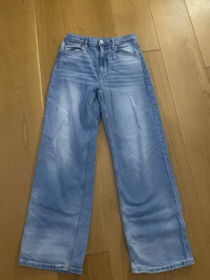 Ljusblå wide jeans med raka ben - Säljer ett par ljusblå jeans med bred passform och raka ben. Klassisk femficksmodell med knapp och dragkedja i midjan. Jeansen har en avslappnad look och är tillverkade i mjukt denimtyg.