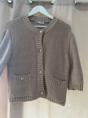Beige stickad kofta från Zara XL - Är storlek XL men känns mindre i storlek så skulle passa en s-m Säljer en beige stickad kofta från Zara i storlek XL. Koftan har grovstickad struktur, rund halsringning, guldfärgade knappar framtill och två fickor med knappdetaljer. Perfekt för lager på lager under höst och vår