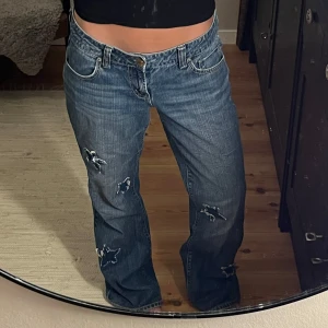 Lågmidjade jeans från American Eagle - (Pris kan diskuteras💗). Säljer en favorit: mörkblå jeans från American Eagle med lite baggy passform och låg midja. Jeansen har stjärnformade patchar på benen i annat denim (5 st fram och 3 st bak), klassiska bakfickor med broderad söm och cool vintagekänsla. Perfekta för en avslappnad streetstil. Det står XL i byxorna men jag är vanligtvis 36-38 och på mig sitter dem väldigt bra. Så XL stämmer inte! 