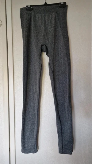 Mörkgrå leggings - Mörkgrå tighta leggings med en sportig vibe, perfekta för träning eller chill. Materialet är stretchigt syntet som andas och sitter skönt mot kroppen. Har använts som underställsbyxor. Har svårt att tyda vad det står för stortlek men skulle tro de är i storlek S. Inga funna skavanker.
