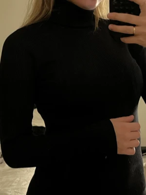 Svart ribbad polotröja Gina Tricot - Säljer en svart ribbad polotröja från Gina Tricot i storlek M. Tröjan har lång ärm, hög polokrage och är i stretchigt, mjukt material som sitter snyggt på kroppen. 