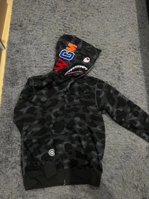 Bape hoodie - Helt ny och oanvänd Bape hoodie, 10/10 skick. Köptes för nått år sedan men jag har inte använt den så jag tänkte att de lika bra o sälja.  Bilderna är tagna i olika ljus. Hör av er vid intresse!