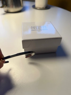 Maison Margiela silverarmband - Snyggt och stilrent armband från Maison Margiela i silverfärgad metall. Armbandet är öppet och har en minimalistisk design med diskret logotyp ingraverad på framsidan. Perfekt accessoar för att lyfta din outfit. Kan går ner i pris under snabbaffär!