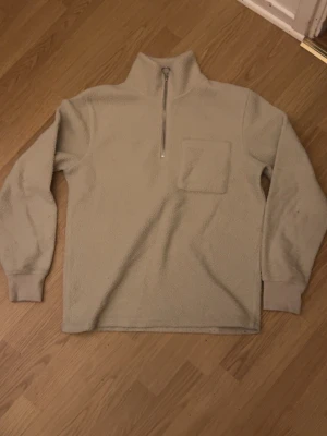 Beige fleece tröja med half zip - Mysig beige fleece tröja med hög krage och half zip framtill. Tröjan har en bröstficka och ribbade muddar vid ärmsluten. Perfekt för kyliga dagar och enkel att matcha med det mesta.