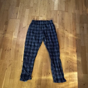 Blårutiga mjukisbyxor i bomull L - Blårutiga mjukisbyxor från Wear M i storlek L. Byxorna har elastisk midja och är gjorda i mjuk bomull, perfekta för chill dagar hemma. Mönstret är klassiskt rutig i mörkblå och grå toner.